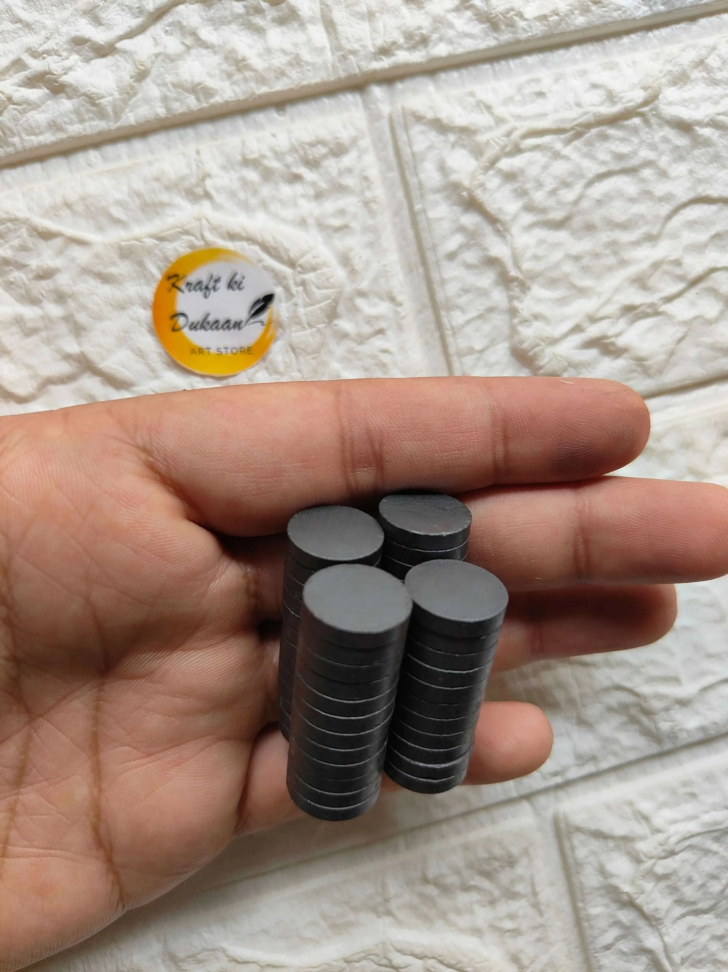 Black round magnets in open hand, showing stacked 15mm x 3mm disc sizes