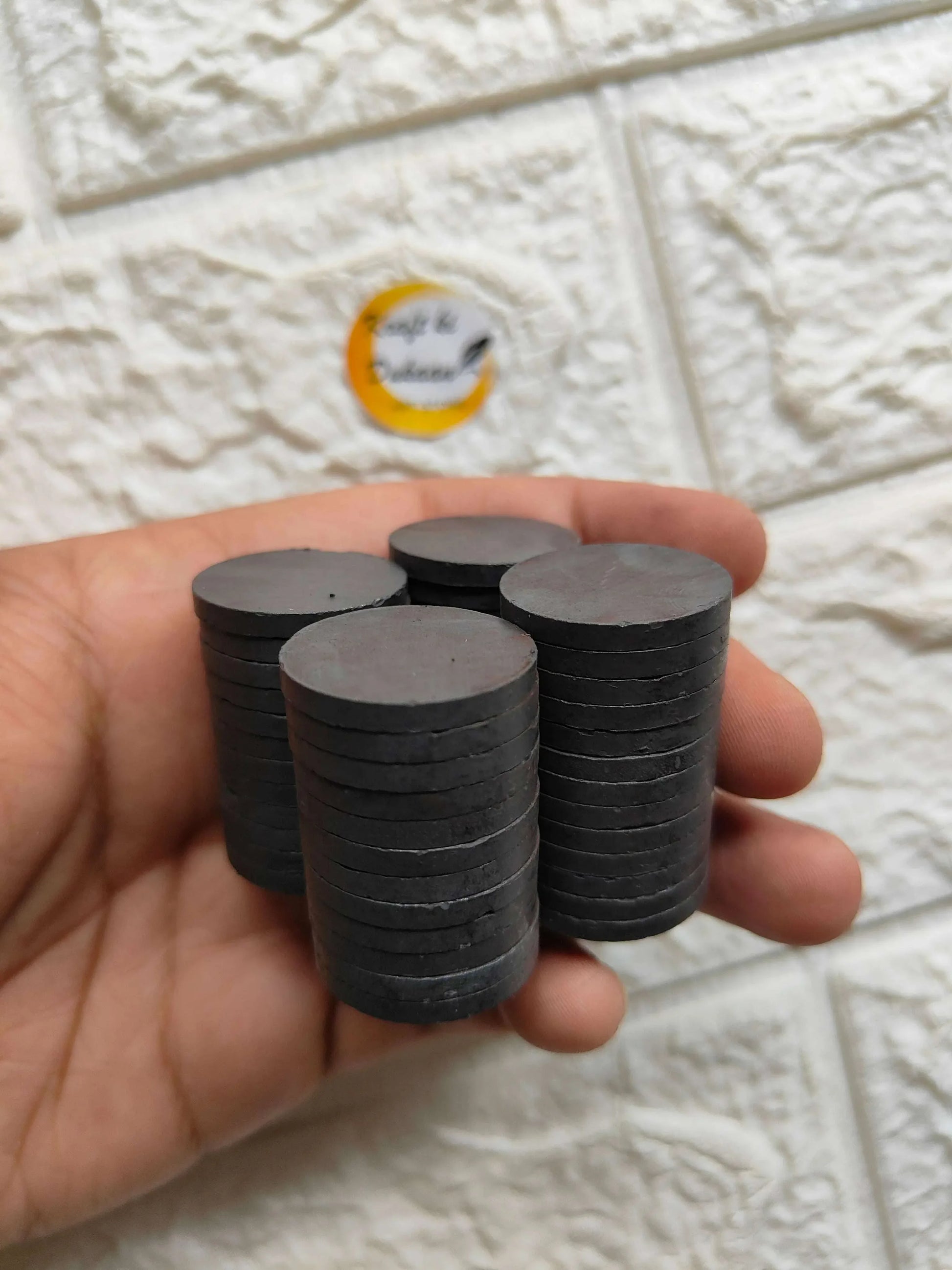 Black round magnet discs held in hand, flat circular faces