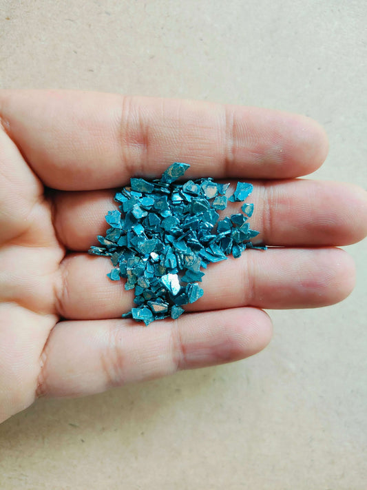 Hand holding blue crystal chips for resin art in a variety of shapes and sizes