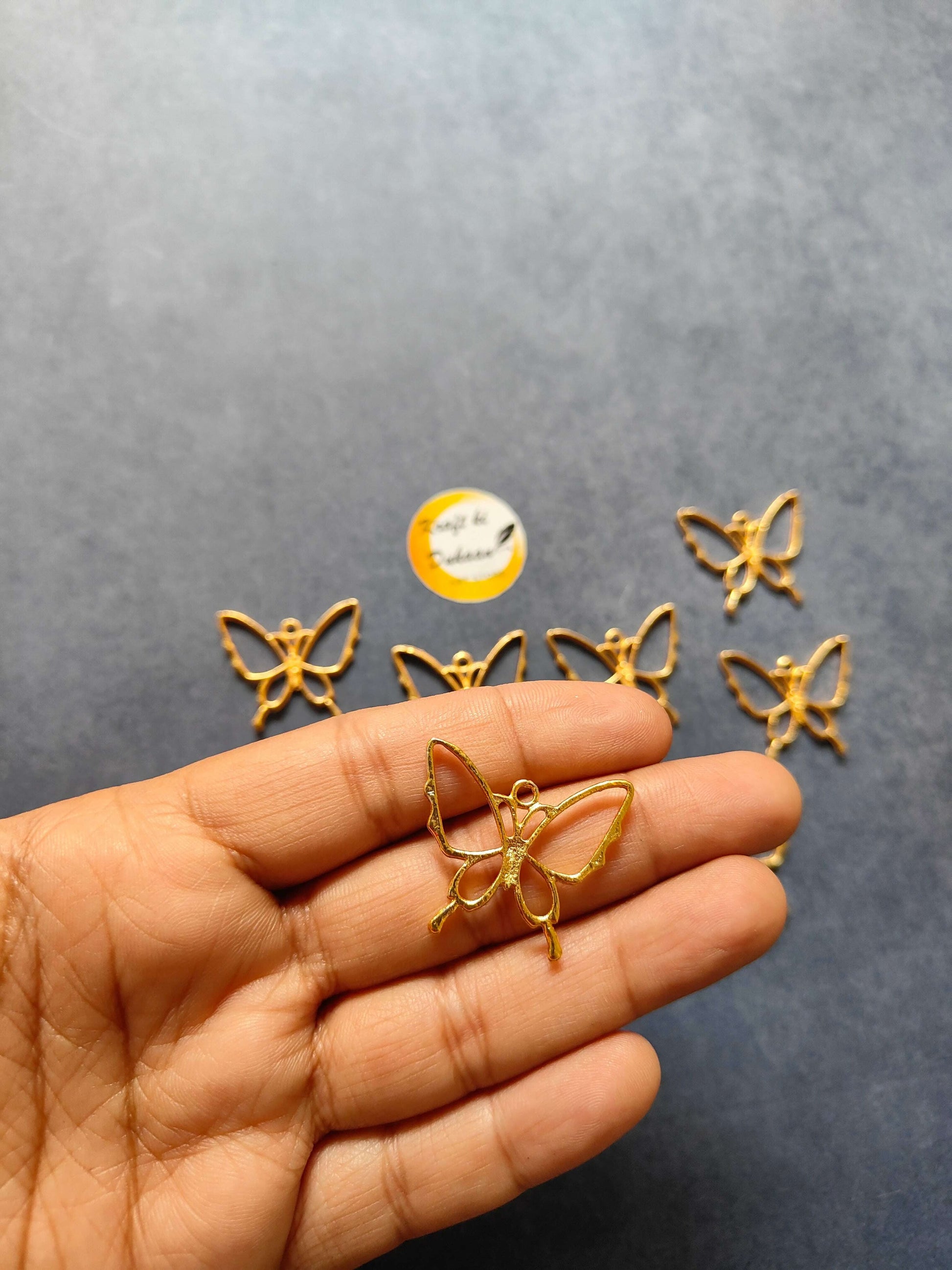 Single butterfly bezel pendant on hand, gold-tone; others laid nearby