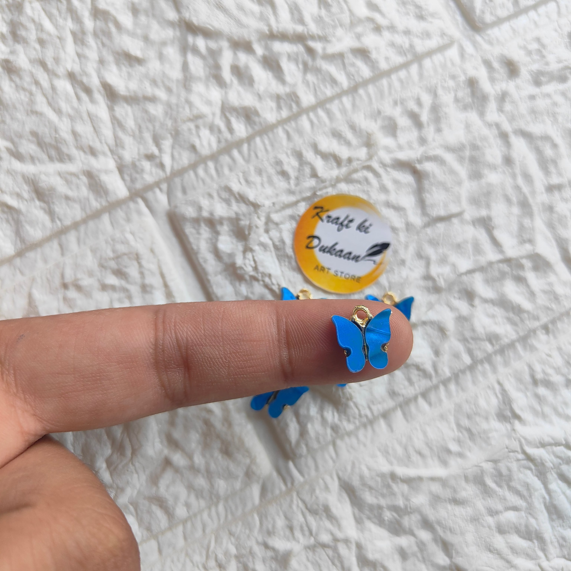 Blue butterfly resin pendant charms displayed on a finger, perfect for crafting and jewelry making