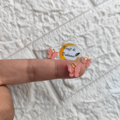 Pink butterfly resin pendant charms displayed on a finger, perfect for jewelry making