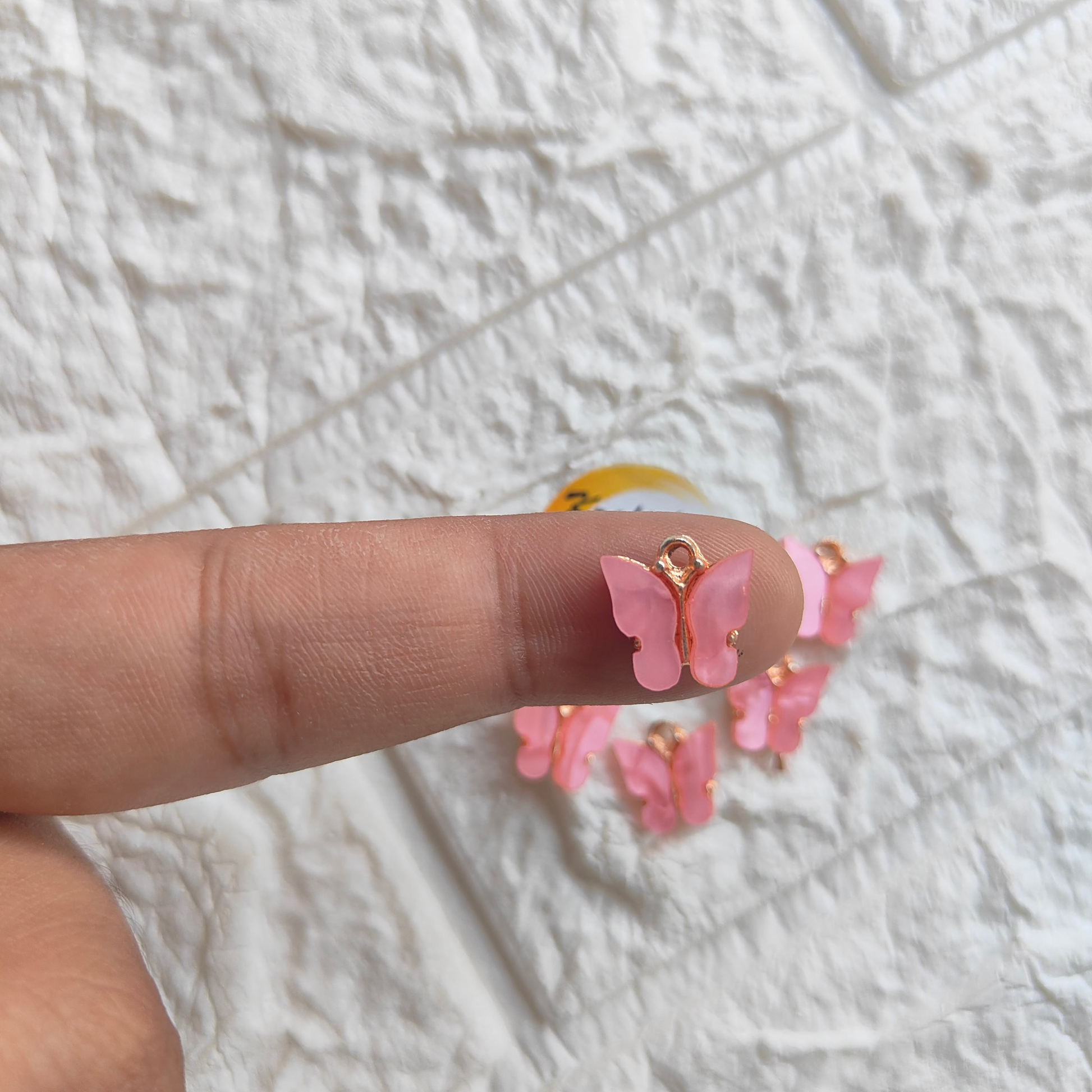 Close-up of pink butterfly resin pendant charms displayed on a fingertip for crafting or DIY projects