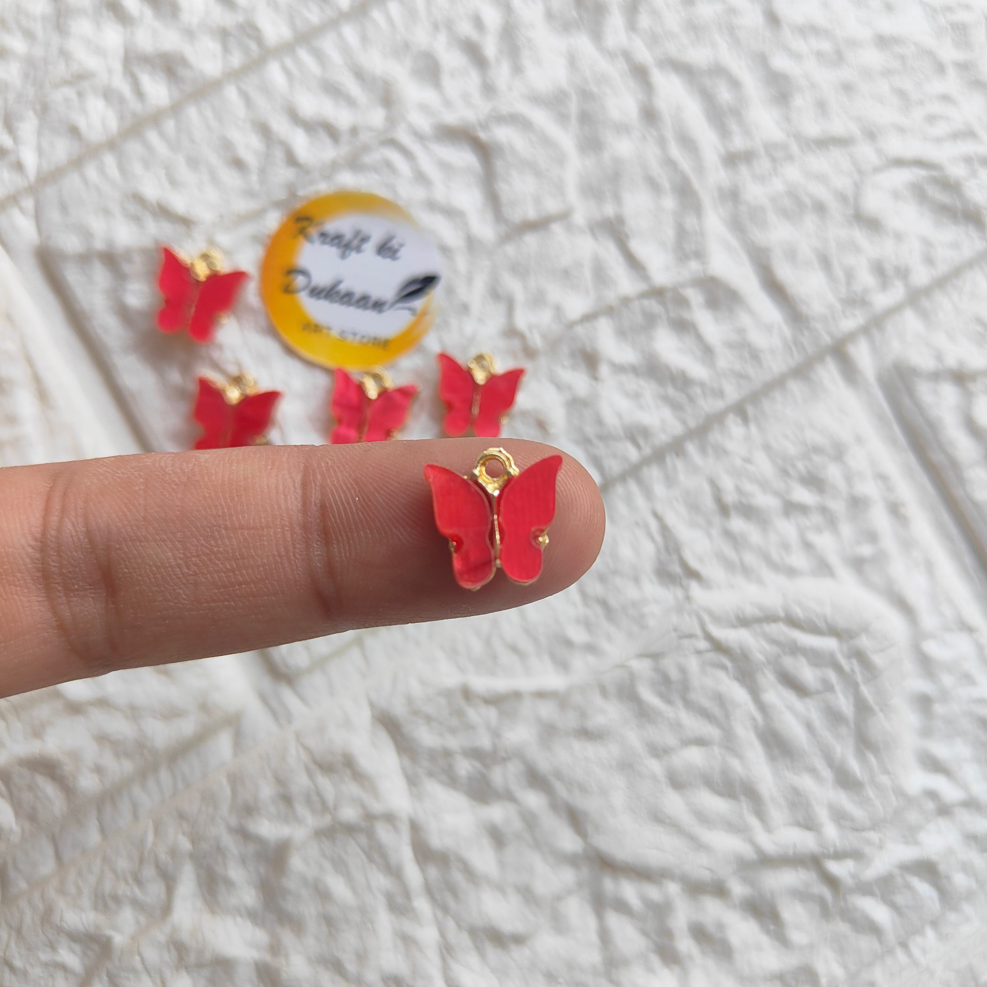 Red butterfly resin pendant charms with gold accents displayed on a finger for crafting projects