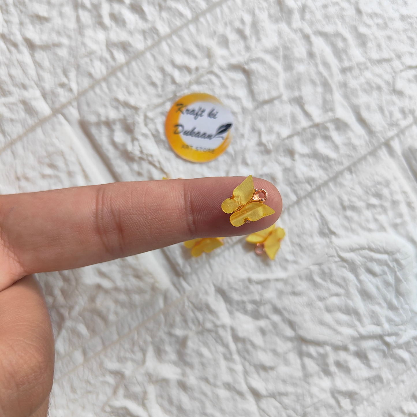 Hand holding yellow butterfly resin pendant charms on textured background by Kraft ki Dukaan