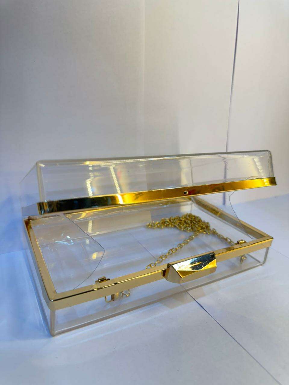 Clear acrylic clutch with gold top bar, central clasp, and thin gold chain