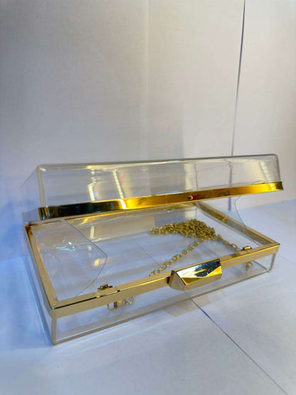 Clear acrylic clutch with gold top bar, central clasp, and thin gold chain