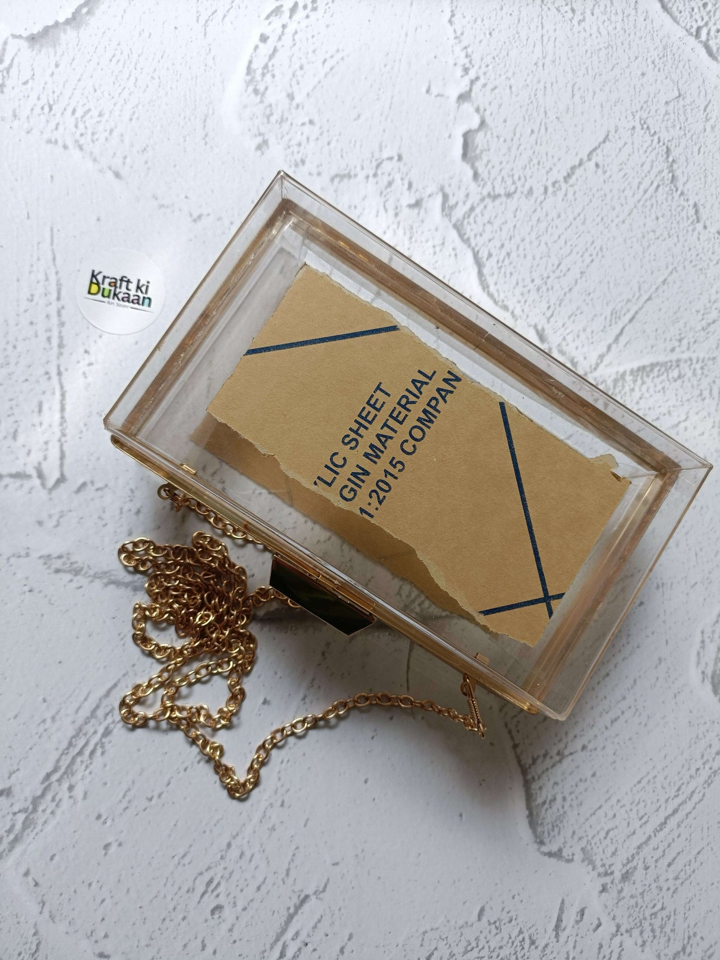 Acrylic clutch bag with gold chain and clasp; label inside the frame
