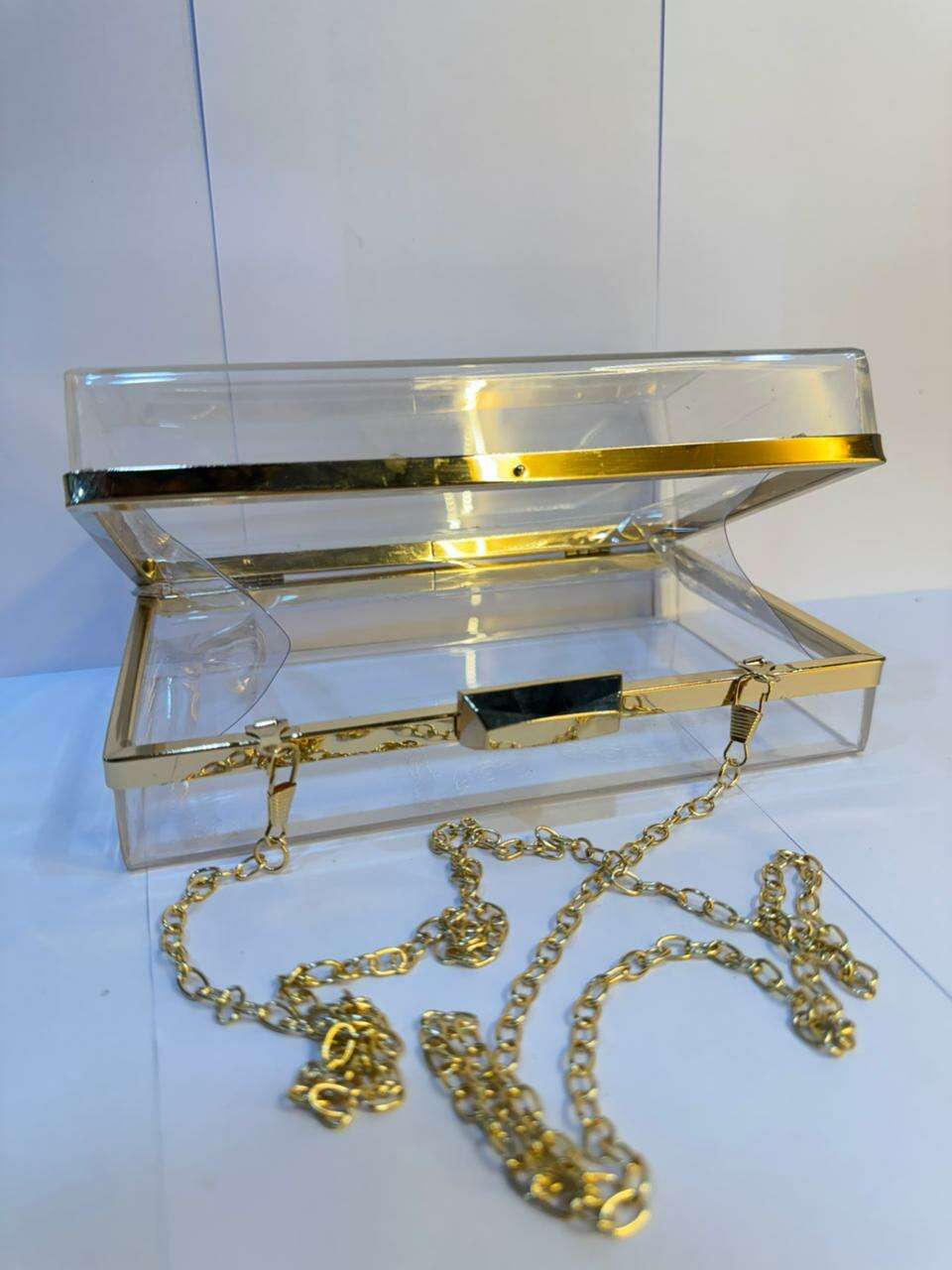 Open acrylic clutch bag with gold clasp and scattered gold chain links