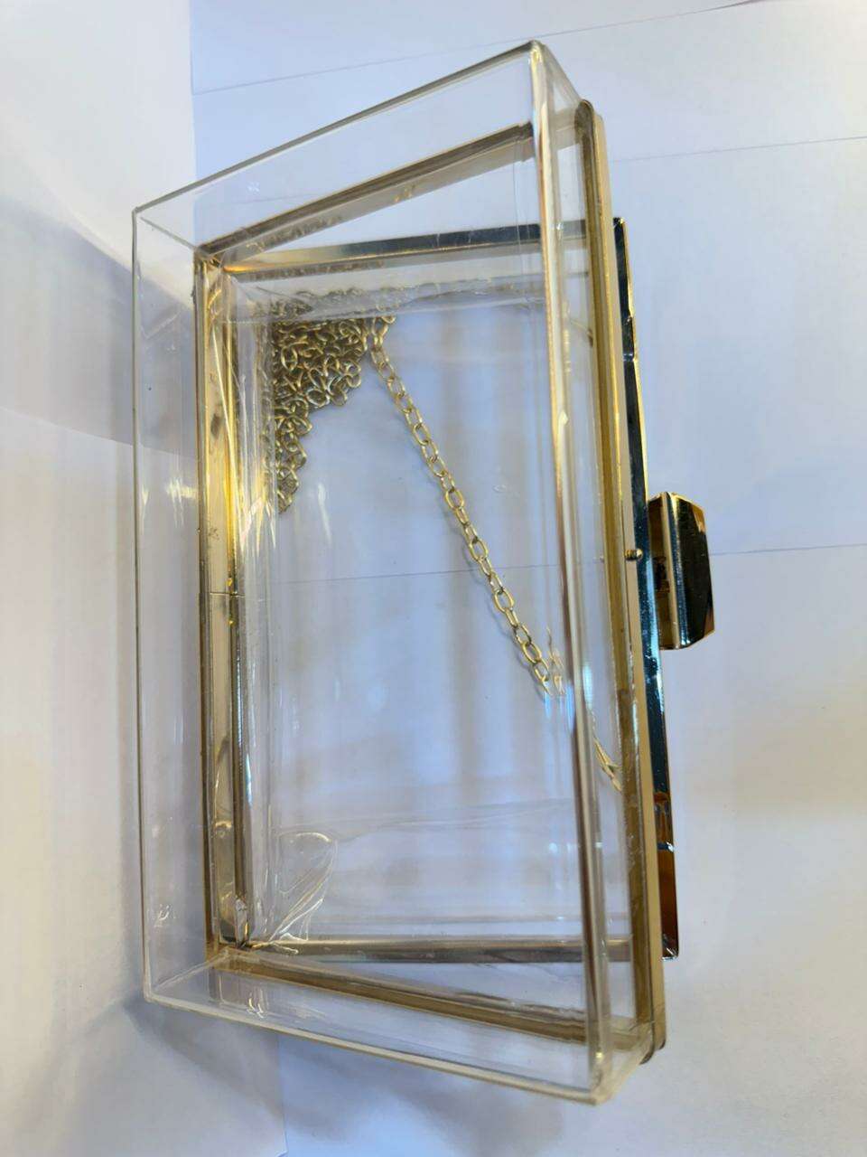 Acrylic clutch bag with gold frame, gold chain strap, and open front