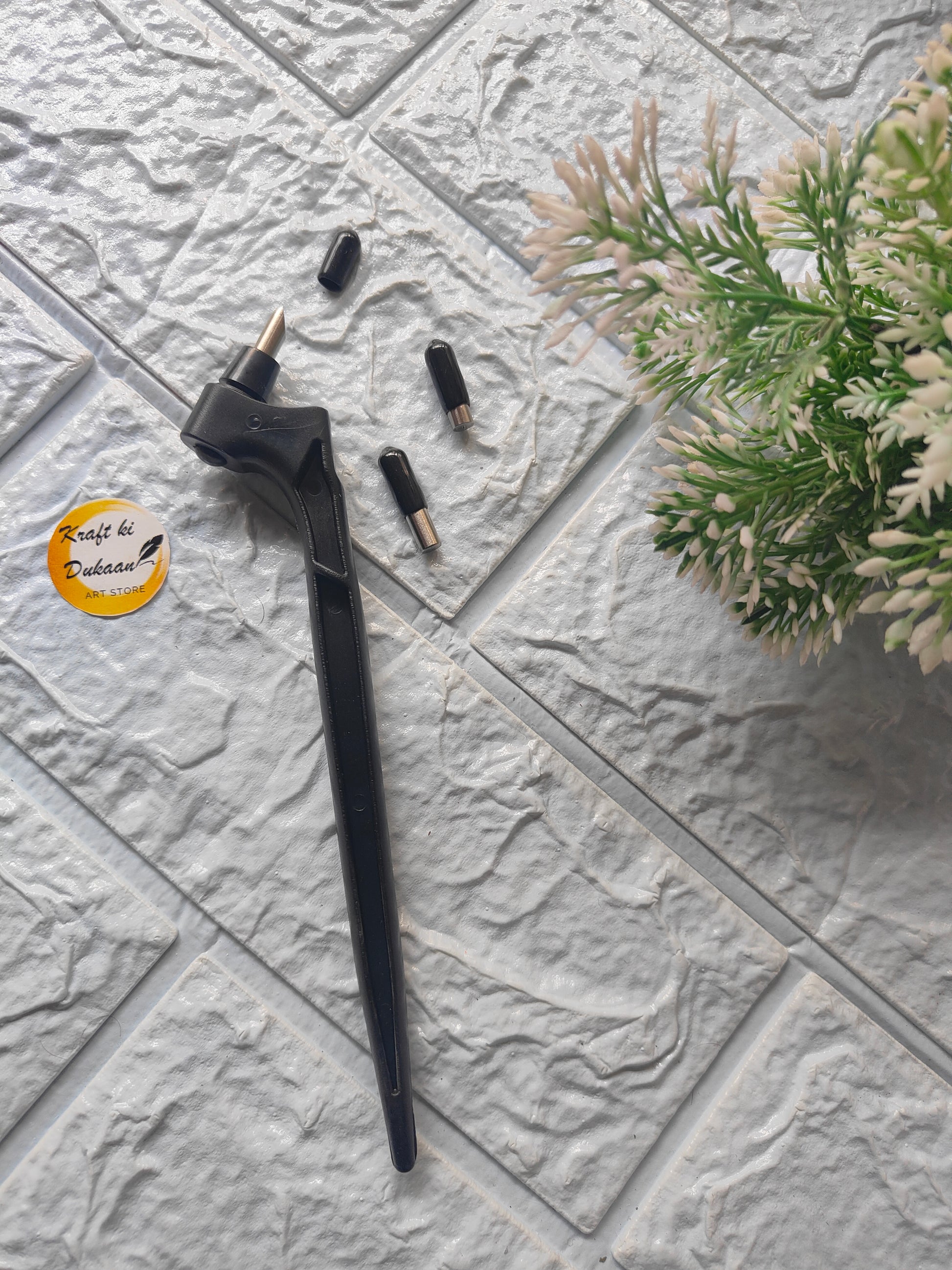 Black 360-degree rotating cutting tool with interchangeable tips on textured gray surface near green plant