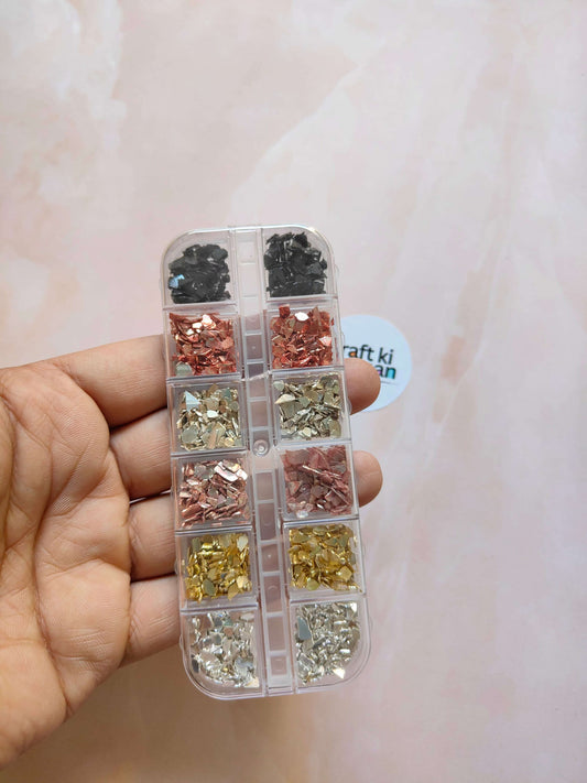 Handheld clear case with compartments of black, rose, gold, and silver stone crystal chips