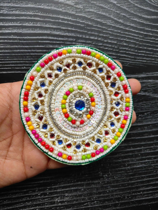 Beaded round patch held in hand: blue gemstone center, rainbow beads and gold details