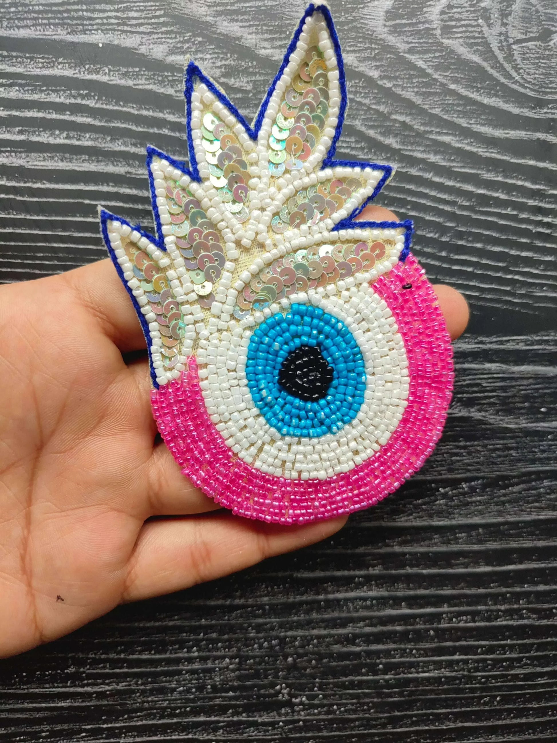 Decorative eye bead patch with blue outline wings, pink base, turquoise center eye
