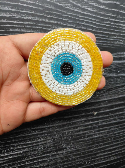 Yellow circular beaded eye patch with blue ring and black center, white border