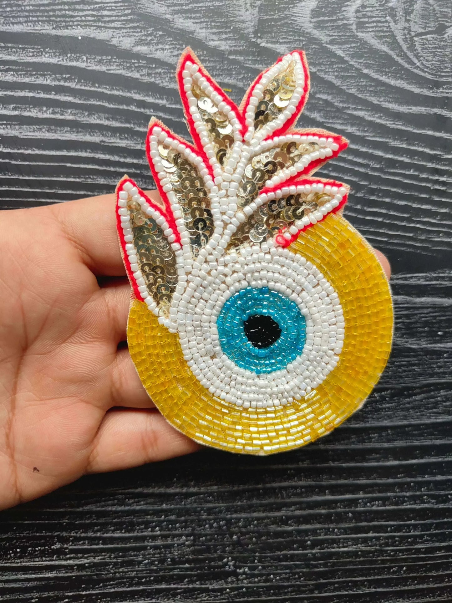 Decorative eye bead patch with gold sequin wings, yellow base, blue center eye