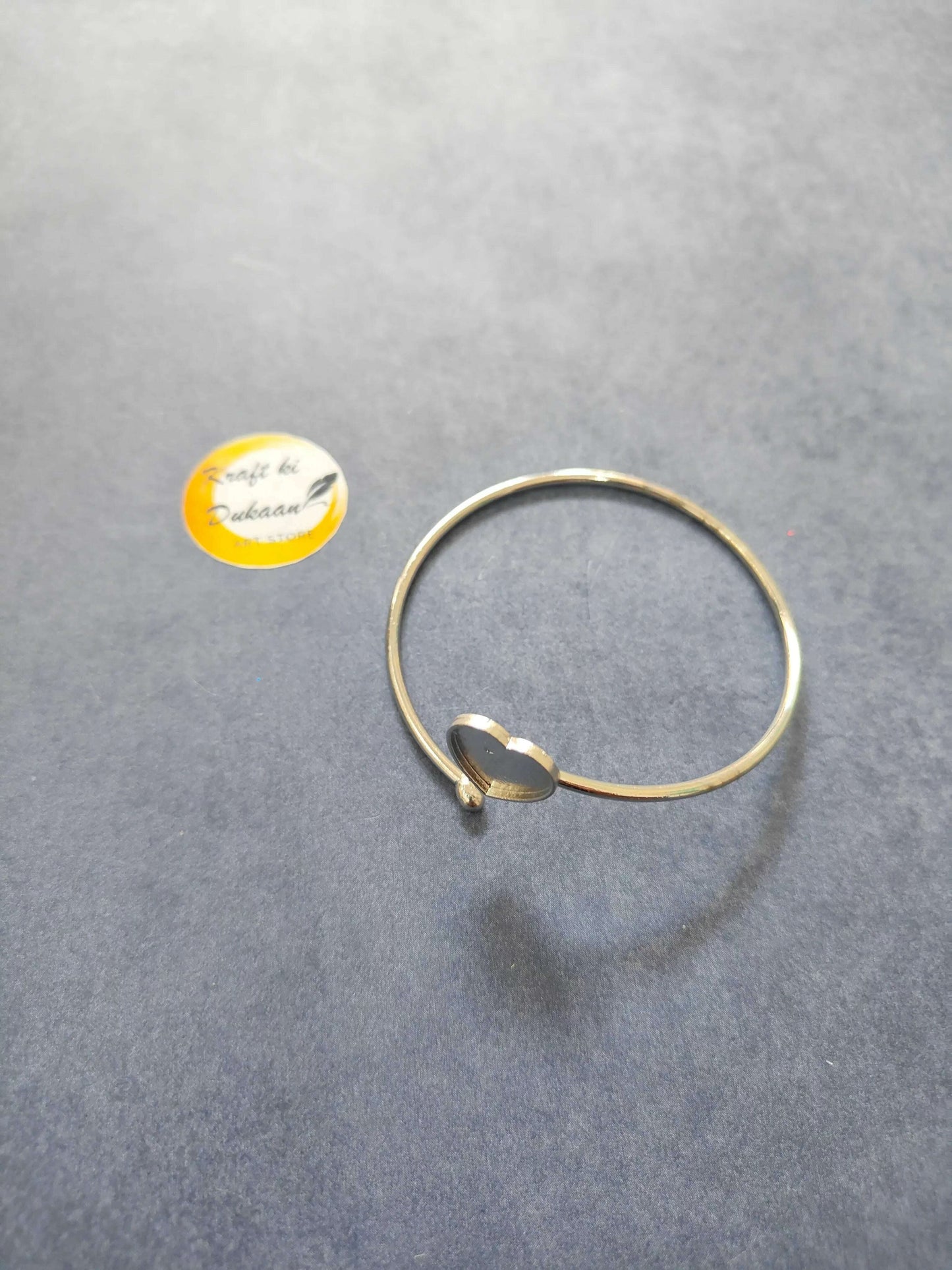 Gold-tone bangle bracelet with a small heart clasp and dark center accent.
