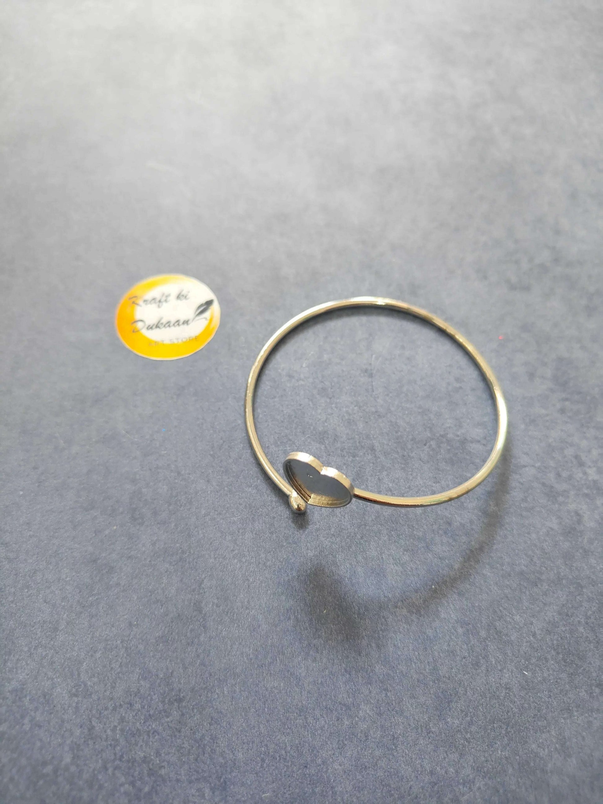 Gold-tone bangle bracelet with a small heart clasp and dark center accent.