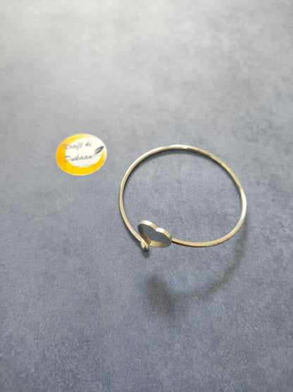 Gold-tone bangle bracelet with a small heart clasp and dark center accent.