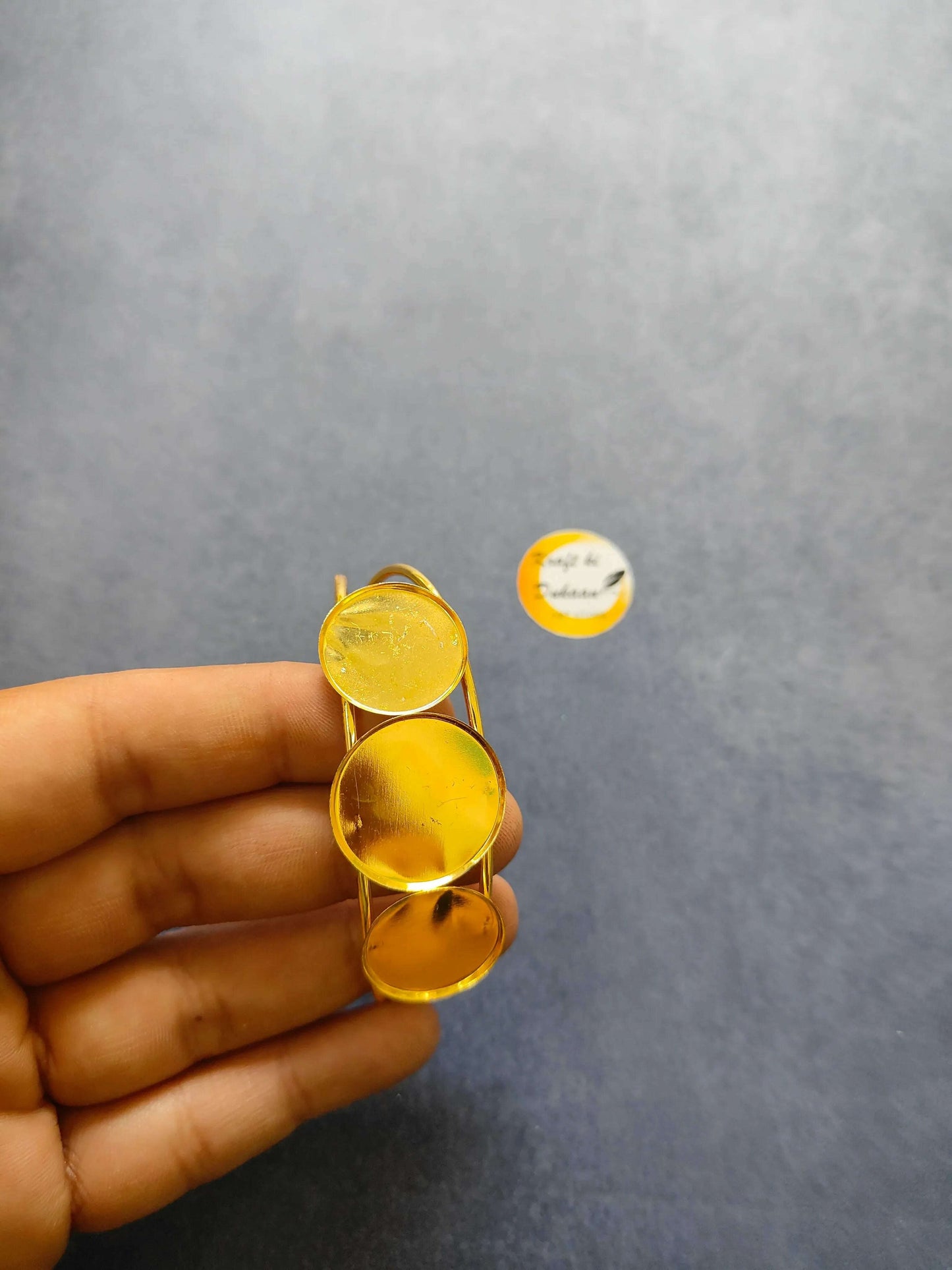 Golden bracelet held in hand; three oval amber stones on a curved metal frame