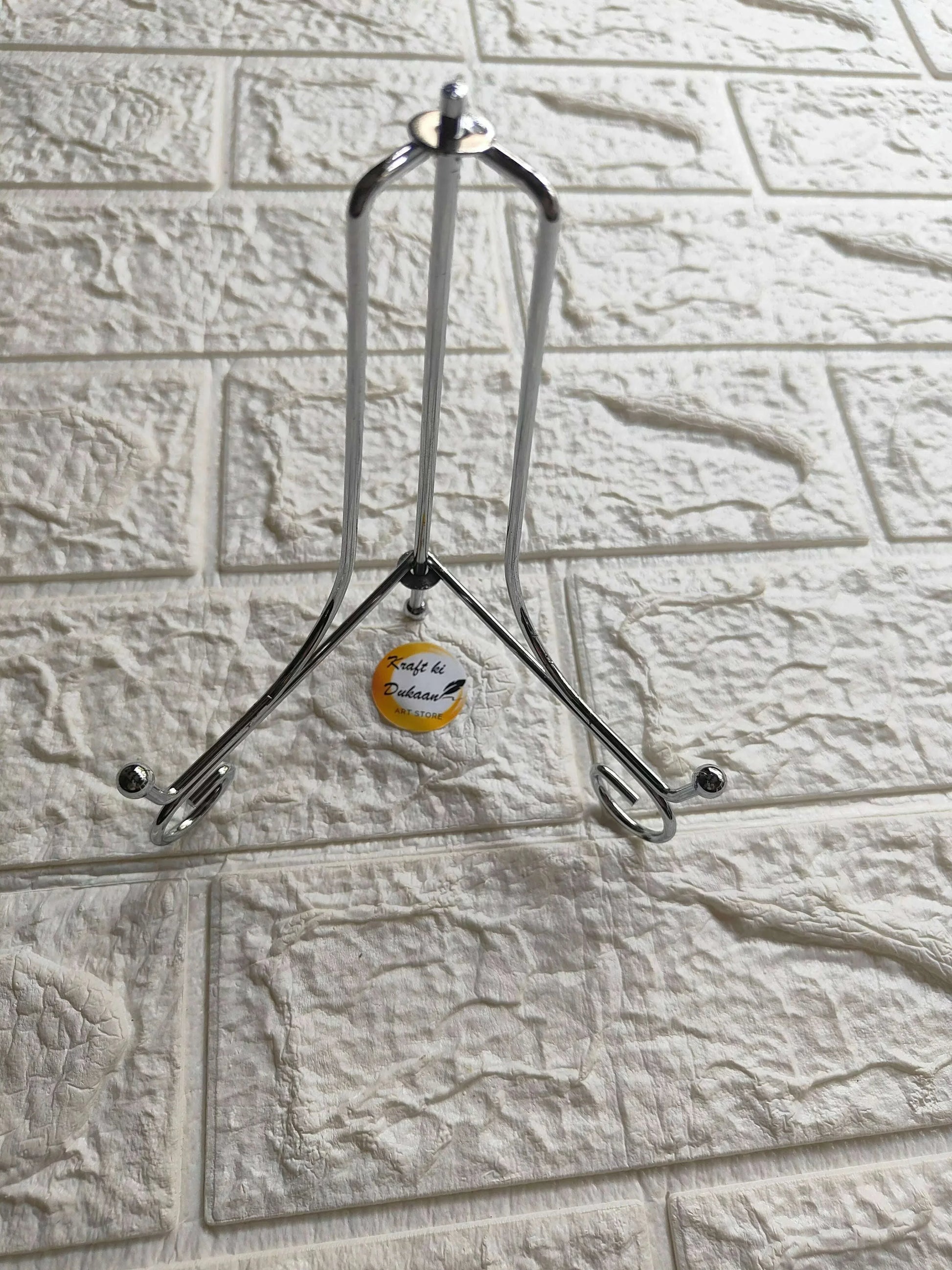 Silver folding metal stand with top handle loop and three support feet