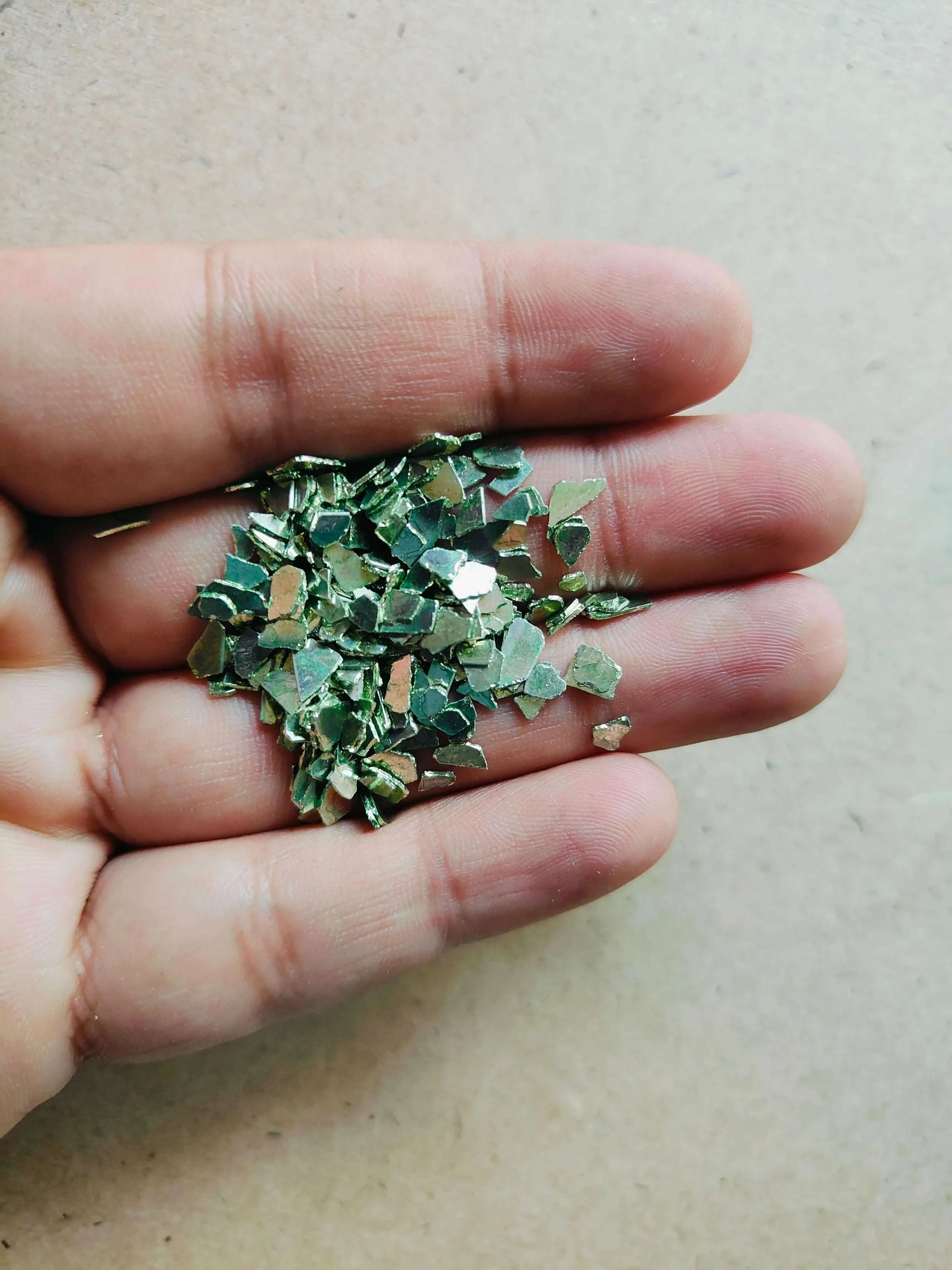 Hand holding shimmering green crystal chips for resin art showcasing small, reflective pieces