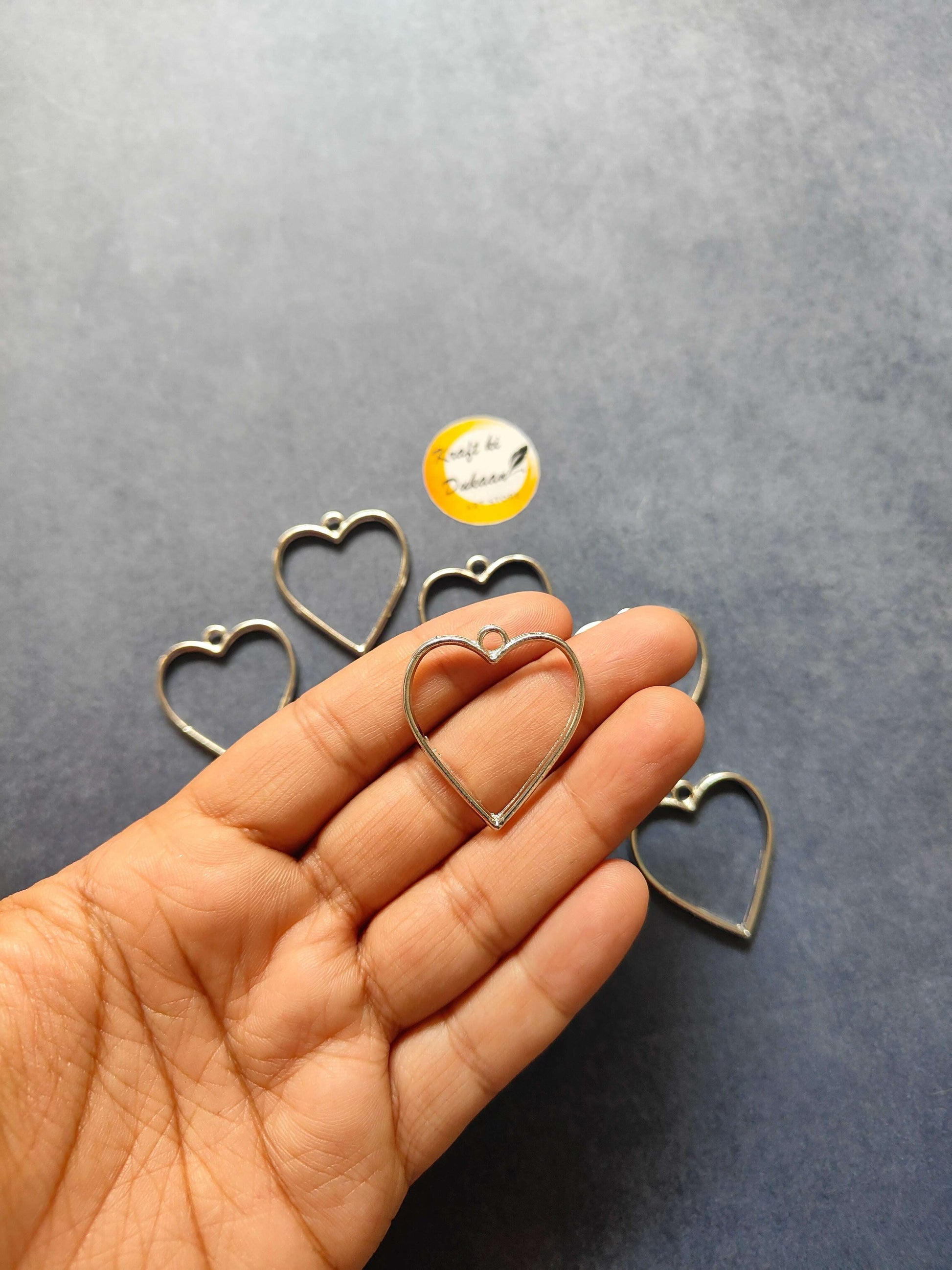 Two gold heart bezel pendants in hand, part of the Heart Plain Bezel 10PC set