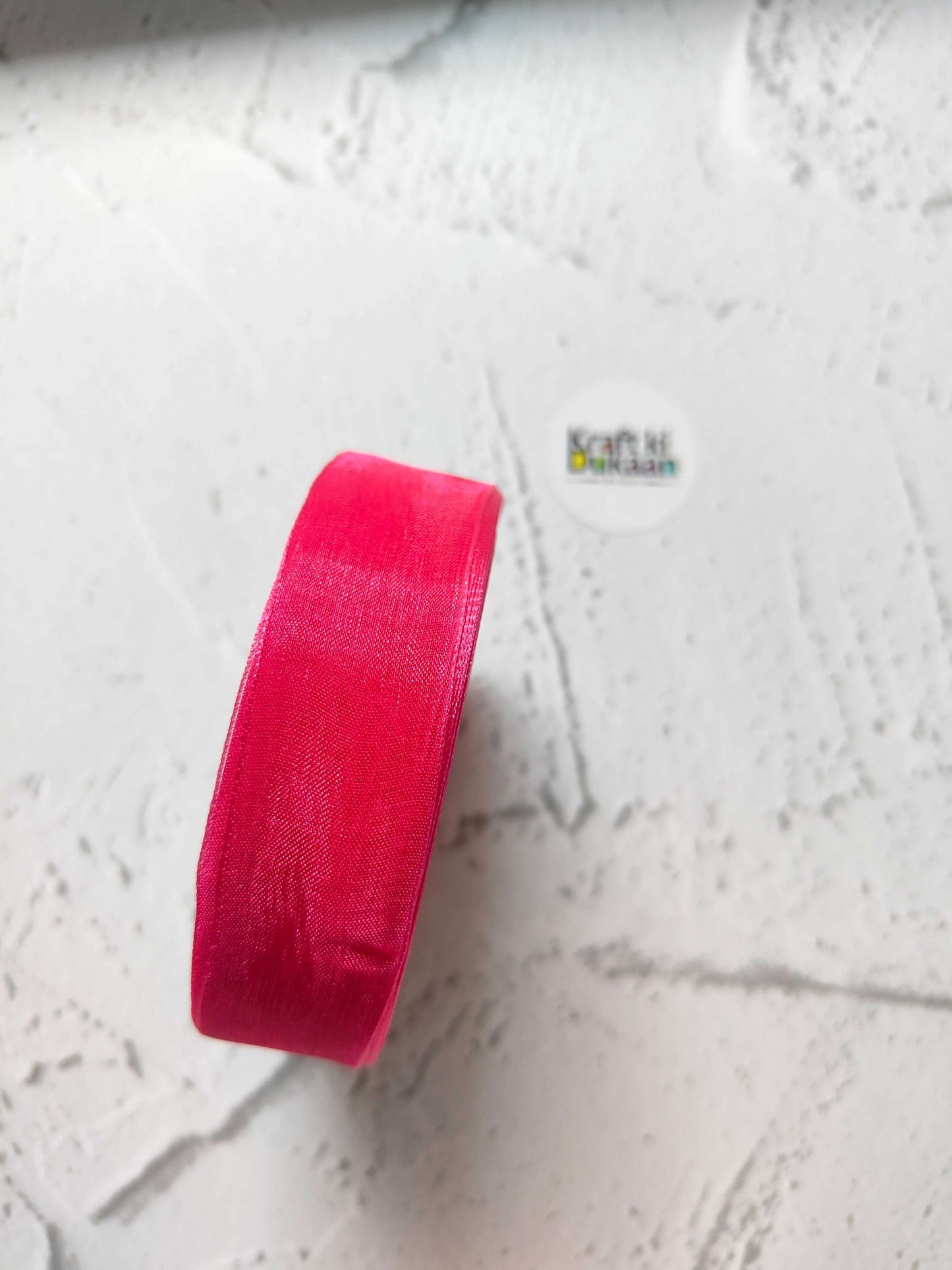 Red organza ribbon roll, narrow sheer strip with woven texture.