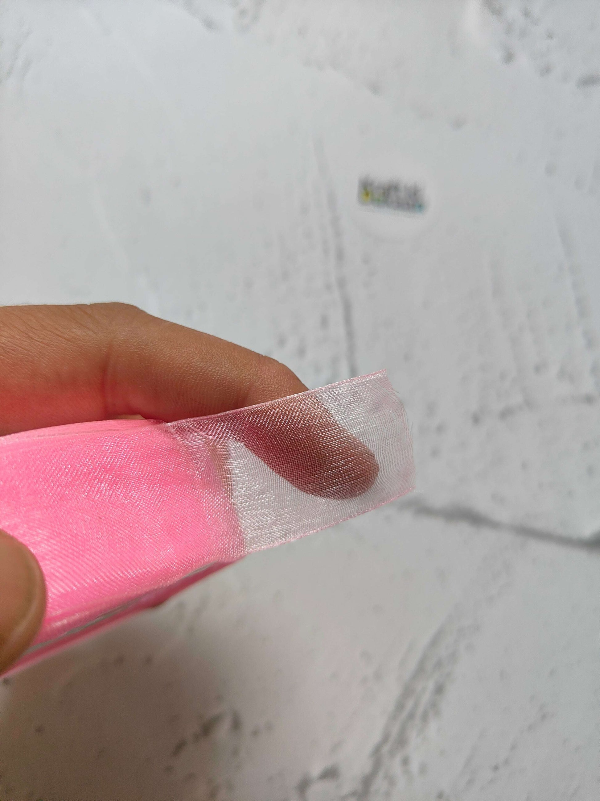 Pink organza ribbon end held in hand, sheer and lightweight mesh weave.
