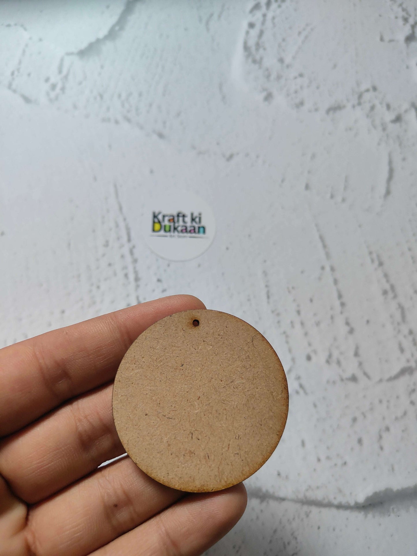 Round MDF craft tag with small top hole, held in fingers, natural brown
