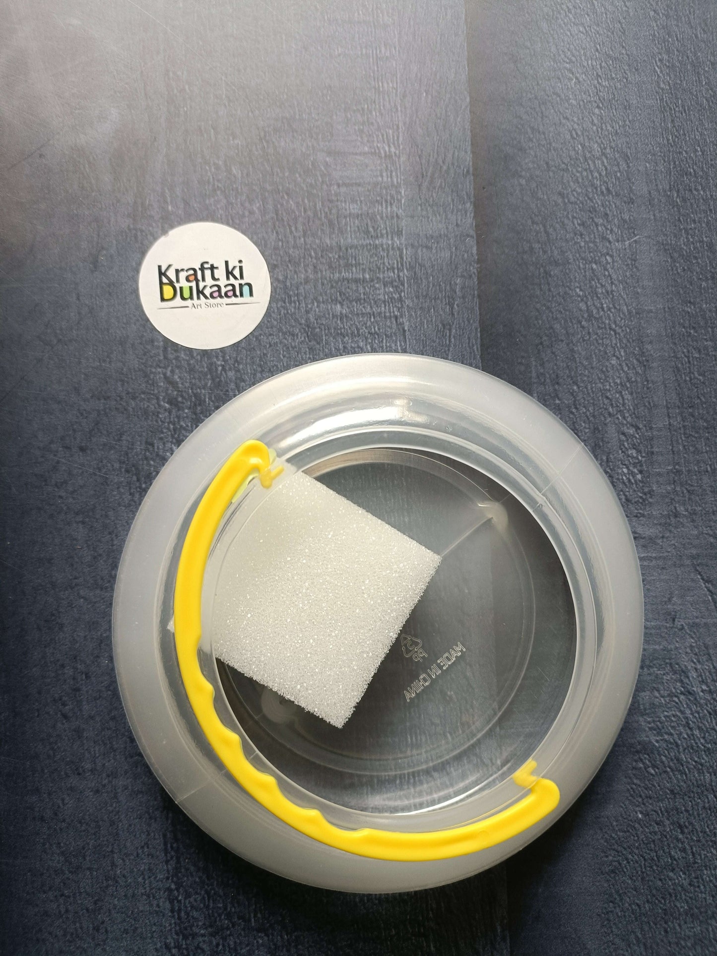 Paint brush wash bucket with yellow handle; clear circular tub containing a white sponge.