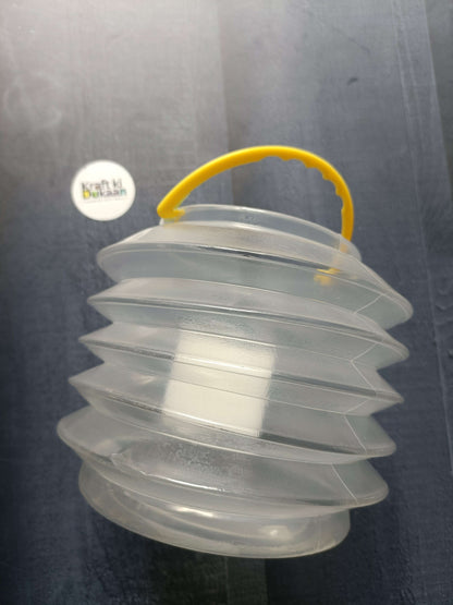Foldable paint brush wash bucket in stacked form; clear panels with yellow carrying handle.