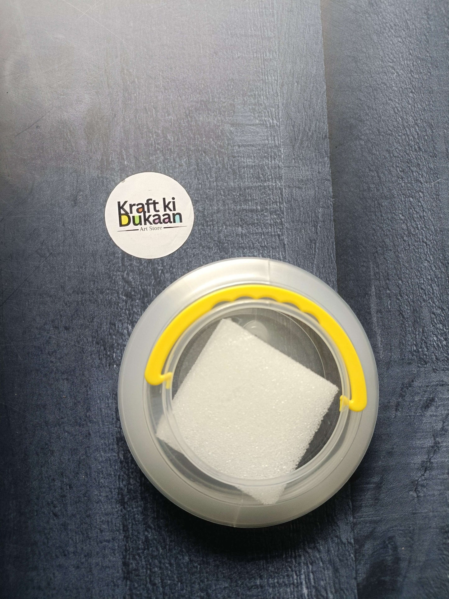 Paint brush wash bucket with yellow handle; white sponge inside clear circular tub.