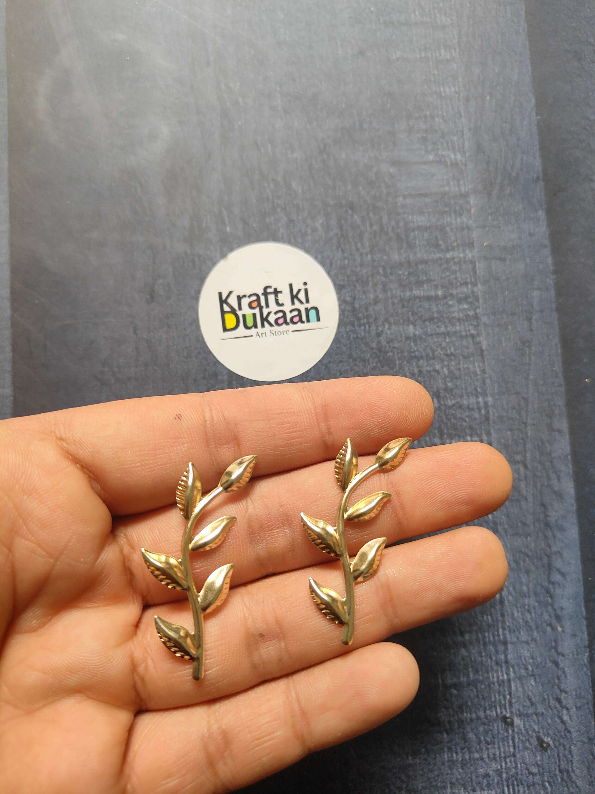 Gold metal leaf embellishments, small pointed leaves on sprig, held in hand