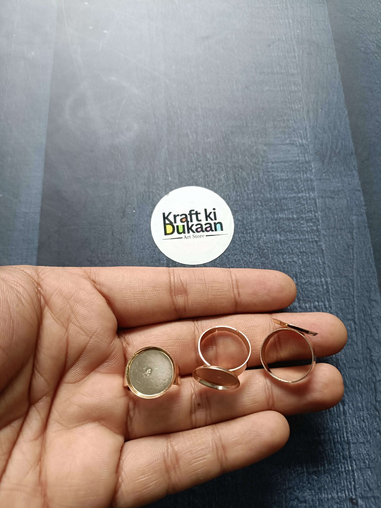 Rose-gold ring bases held in hand, round bezel settings on open bands (4 shown)