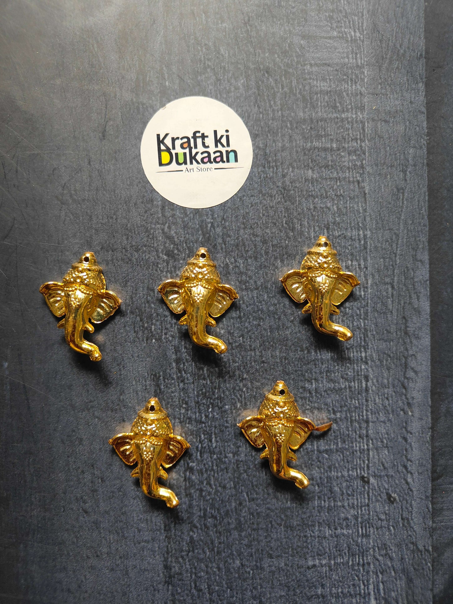 Pack of 10 golden Ganpati face charms, 3.5cm—five shown on dark fabric
