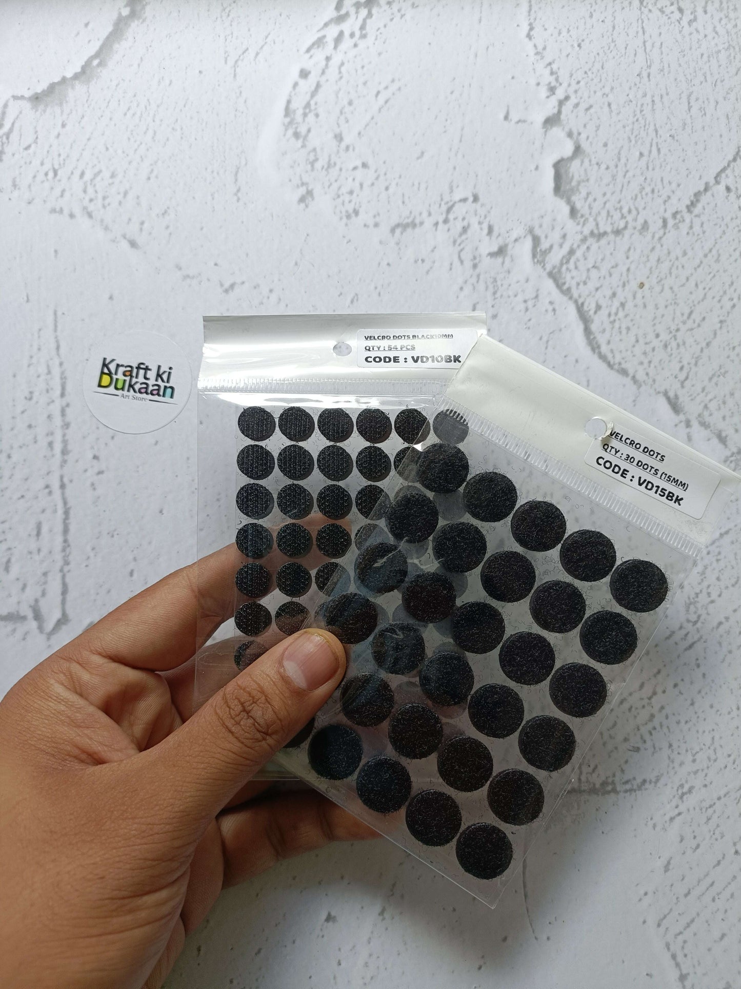Black round Velcro dots on clear backing sheet, held by hand