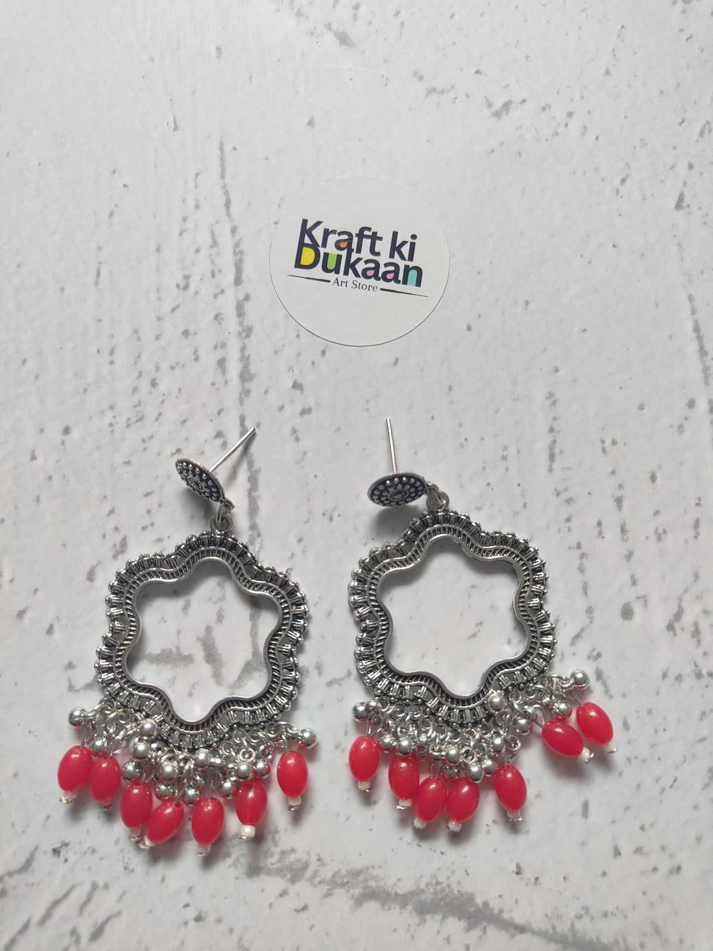 Silver flower jhumka earrings with red bead drops, ornate silver-toned pair