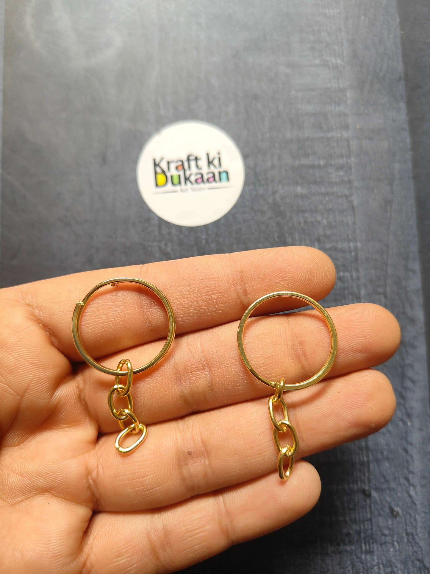 Gold-tone small keychain rings with short chain and clasp, held in hand