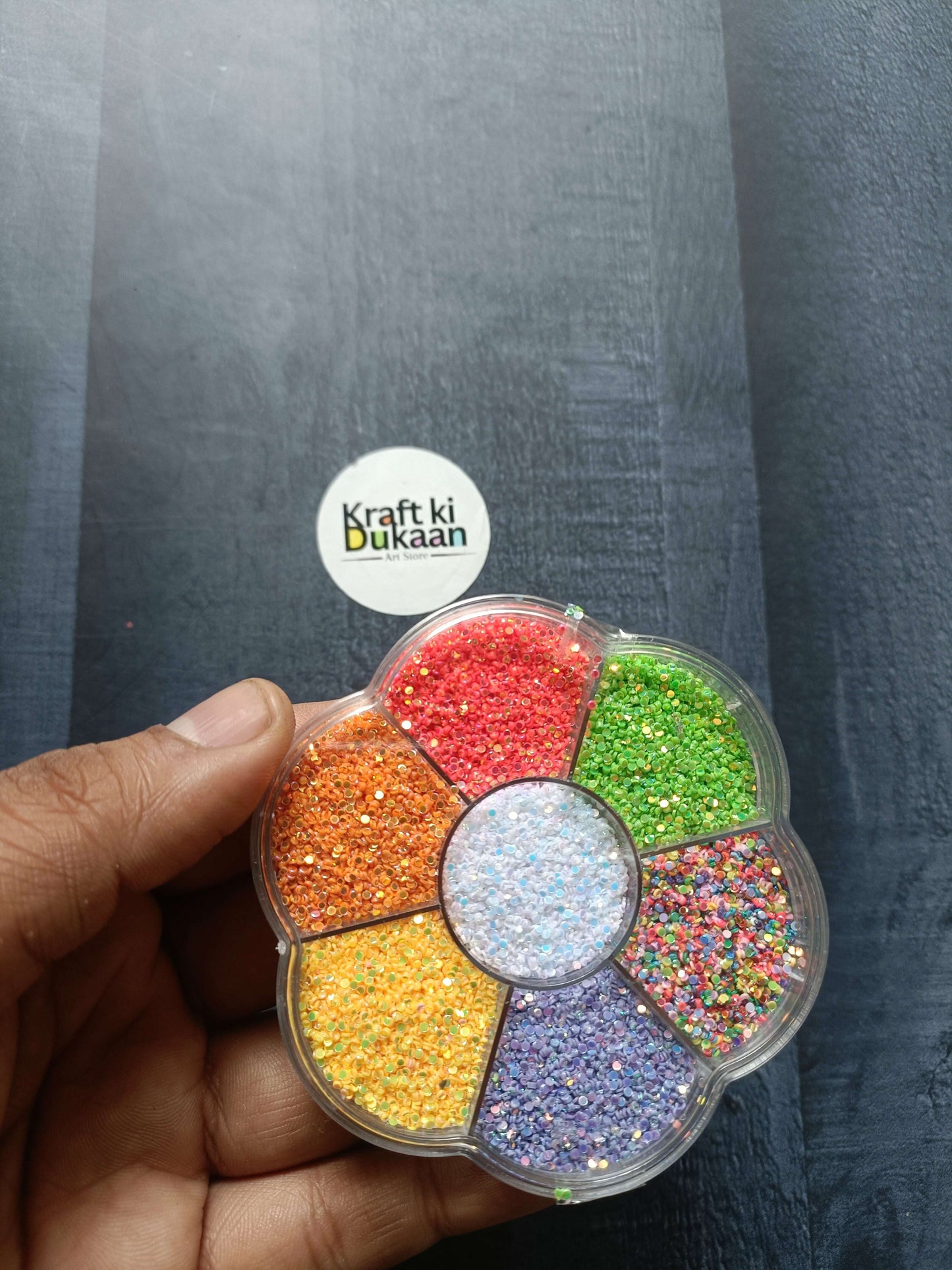 Round glitter box in hand, red, green, orange, yellow and purple glitter in 8 sections