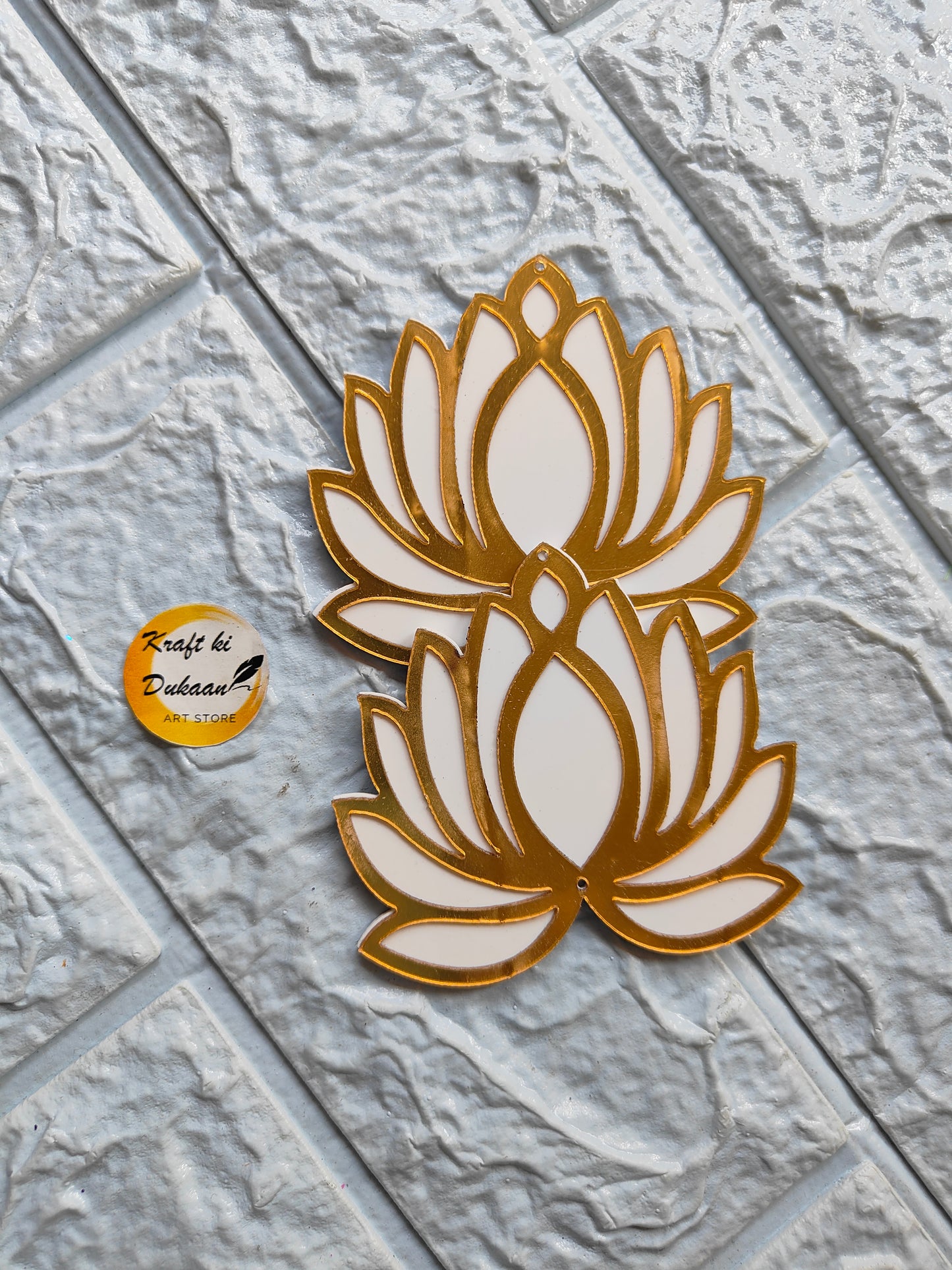 Two golden and white acrylic lotus cutout decorations on textured gray surface from Kraft ki Dukaan