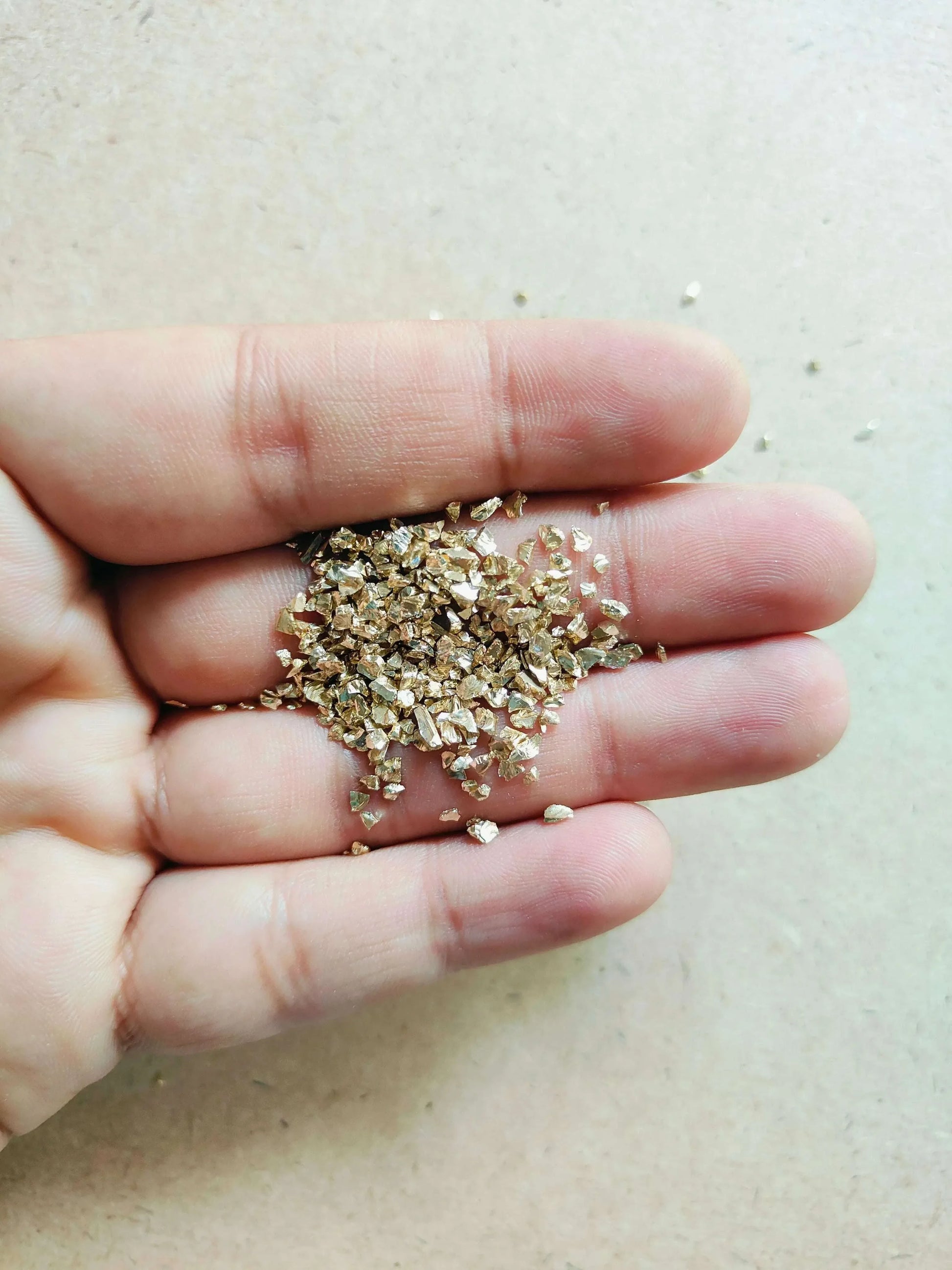Close-up of light gold granules for resin art held in a hand, perfect for crafting projects