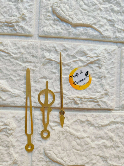 Metal clock hands set in gold, three hands with circular bases on display.