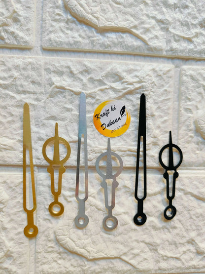 Metal clock hands set: gold, silver-gray, and dark/black pieces on a board.