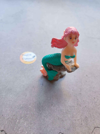 Mini mermaid figurine with pink hair and green tail, sitting on rocky base