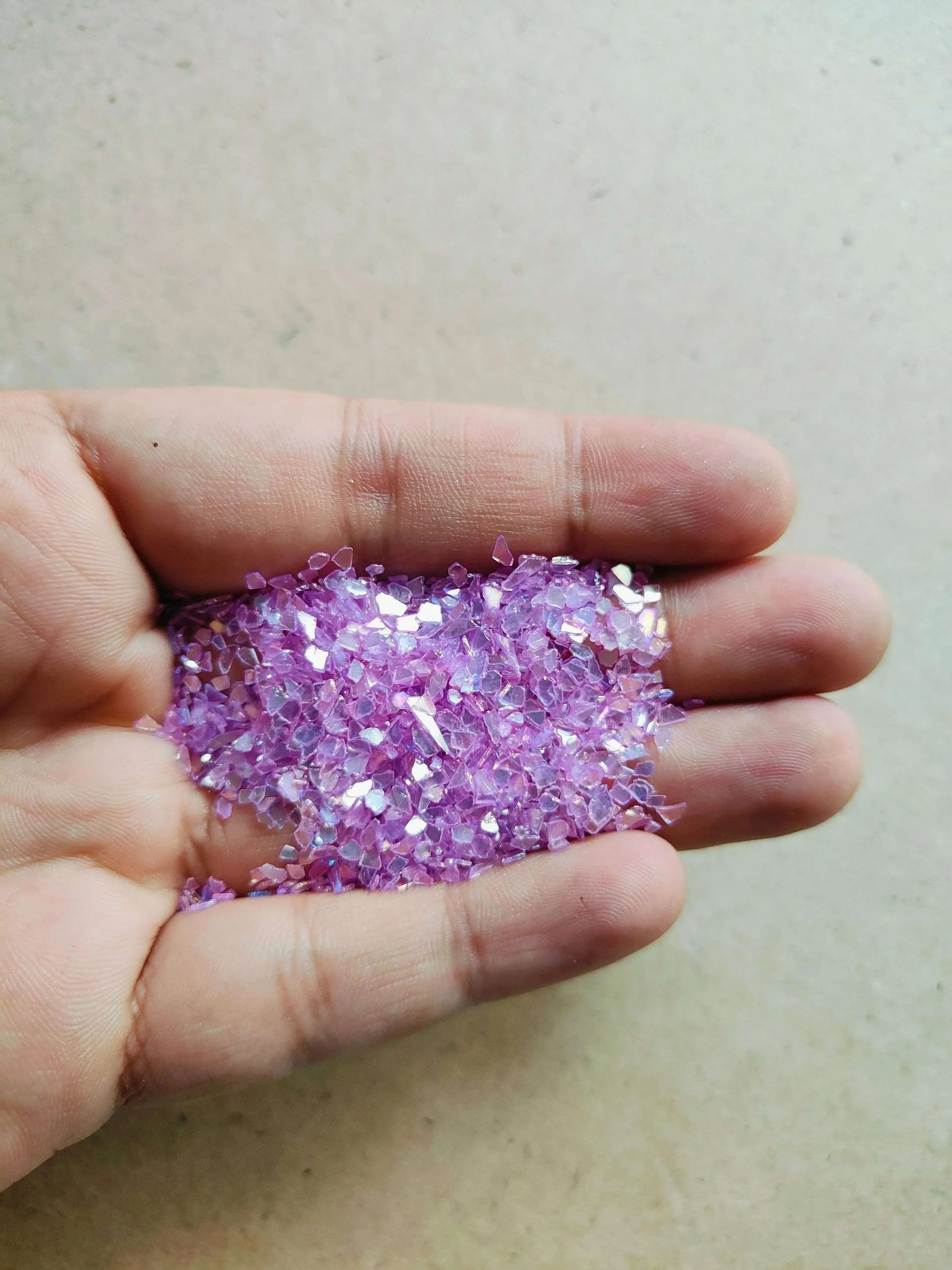 Hand holding pink resin crystals for crafting and decorative purposes