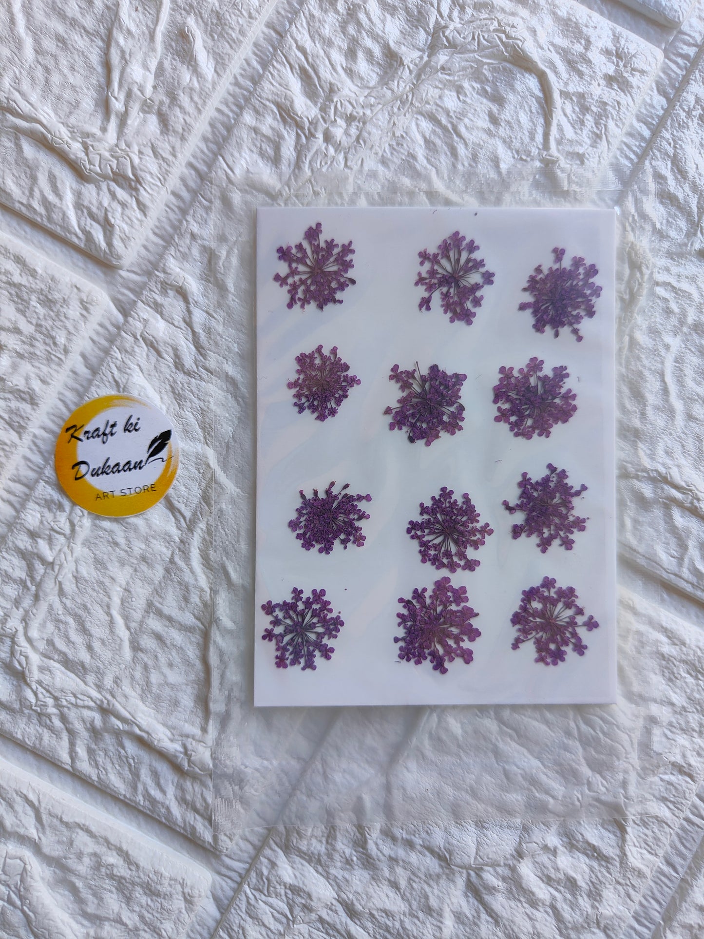 Pressed flower art supplies featuring 12 dried purple flowers on a clear backing sheet
