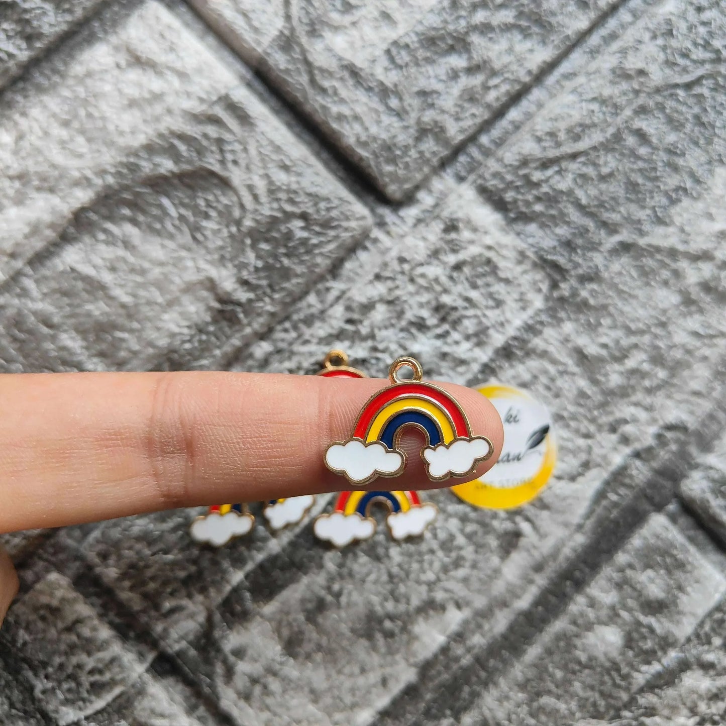 Rainbow metal charm with red-yellow-blue arc and white cloud detail, held in hand