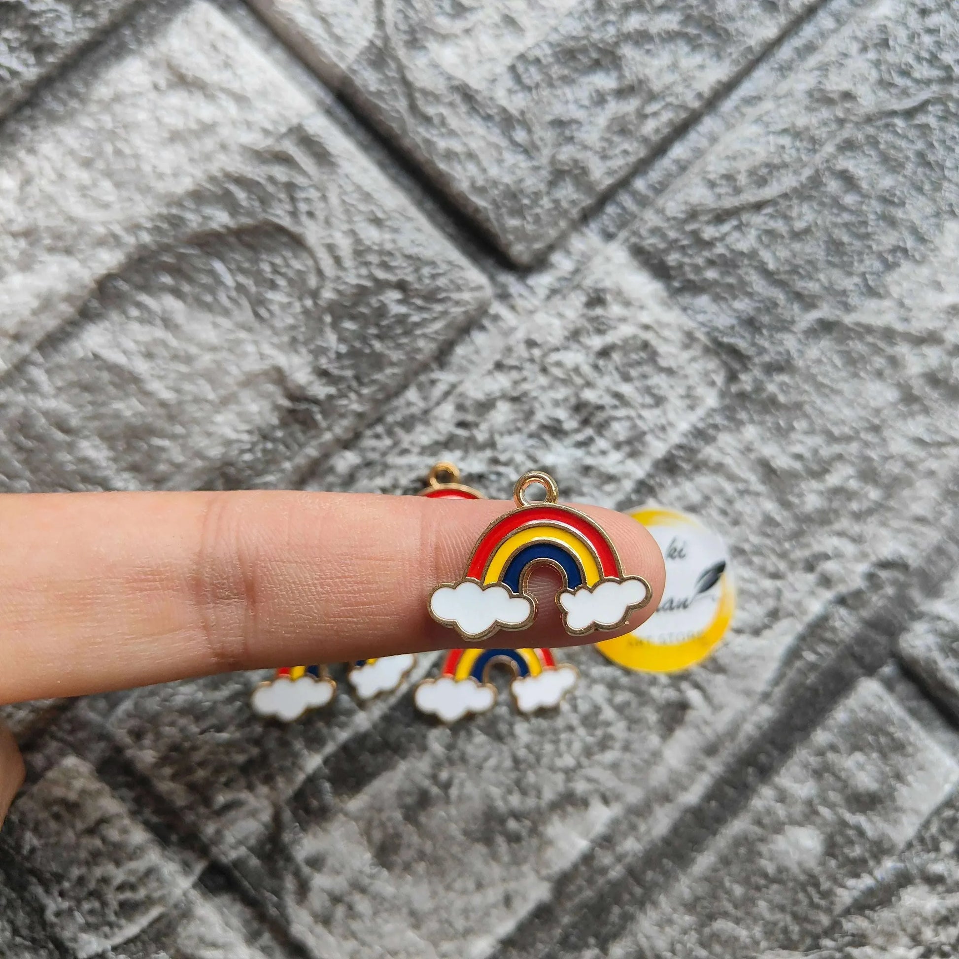 Rainbow metal charm with red-yellow-blue arc and white cloud detail, held in hand