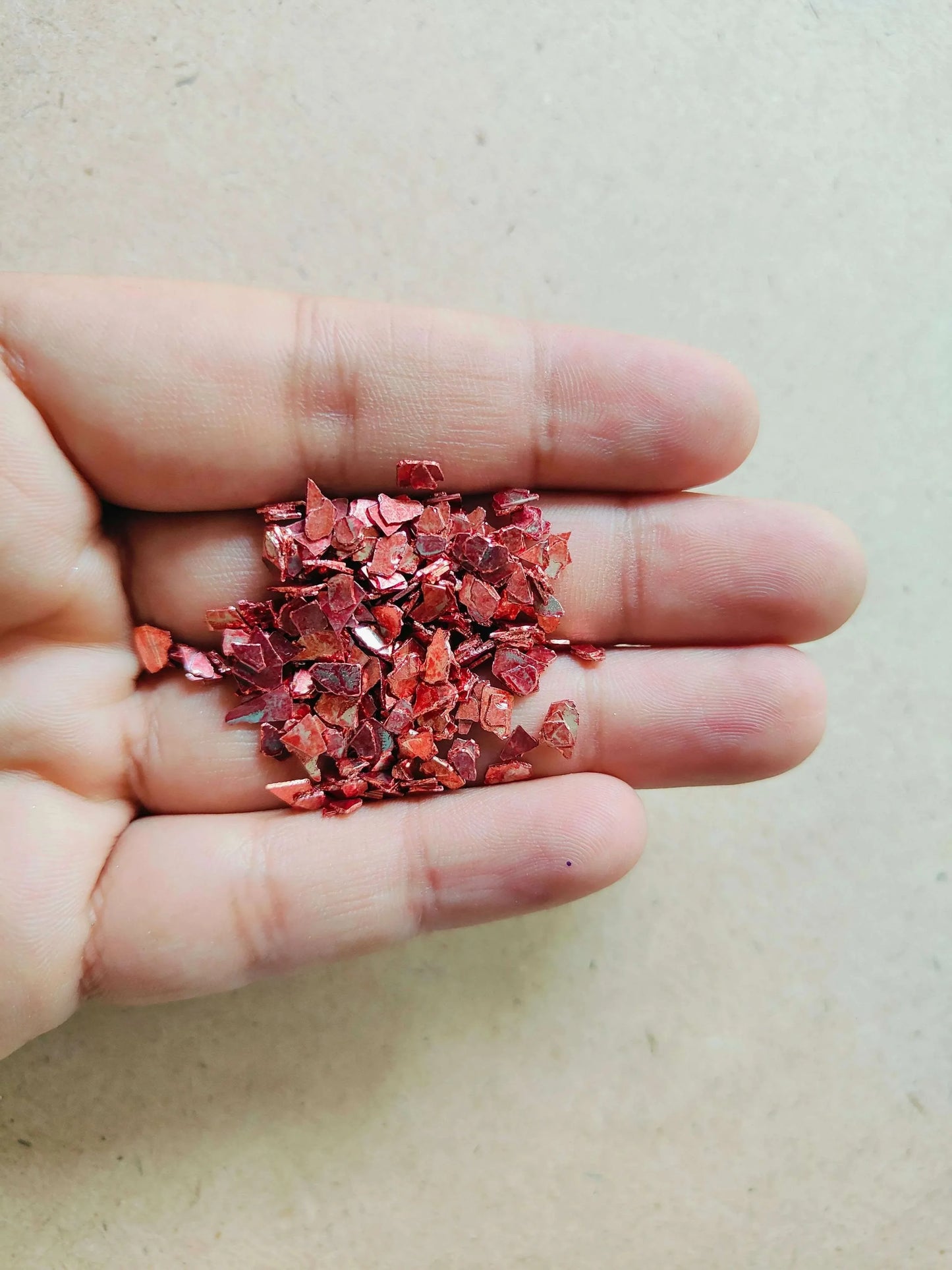 Red crystal chips held in an open hand, glittery small flakes